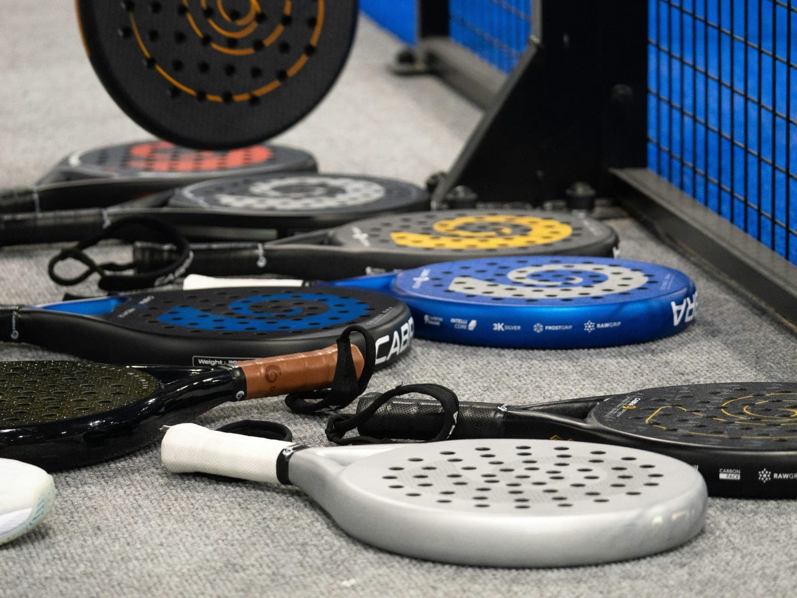 Une douzaine de raquettes de padel posées au sol au bord d'un court